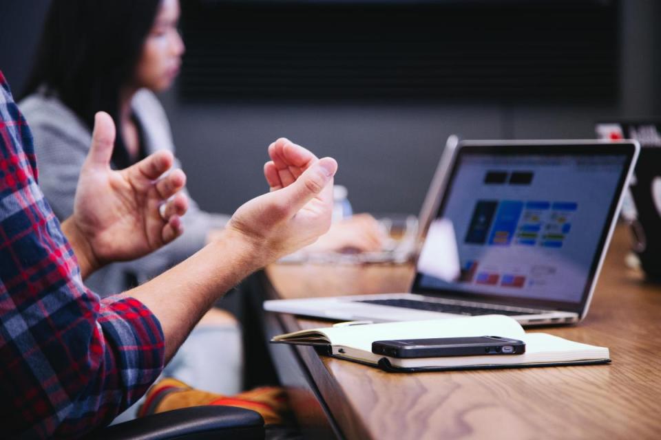 A close up on a pair of gesturing hands in front of an open laptop.