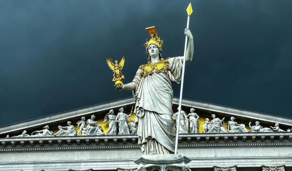 A gold plated statue in front of an ornate government building