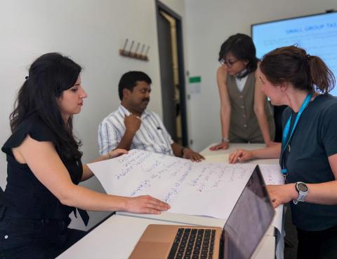 Four people in a classroom gathered around a large piece of paper.