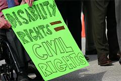 Close up on a person in a wheel chair holding a sign that says "Disability Rights = Civil Rights."