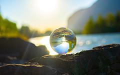 A glass globe sitting on a rock in front of a lake.