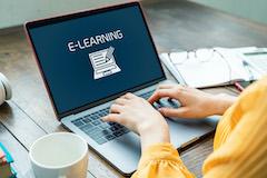 A woman typing on a laptop that says "e-learning" on the screen.